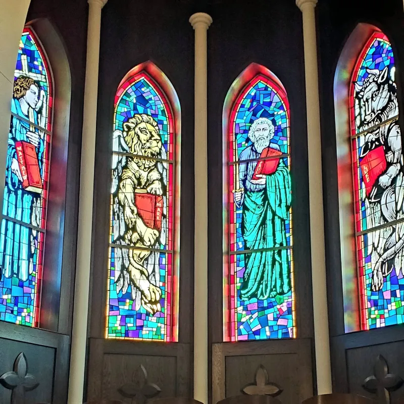 Four tall stained-glass windows in vivid blues, reds, and greens, each portraying a Gospel writer with his symbol
